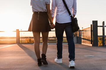 Young couple walking hand in hand on parking level at sunset
