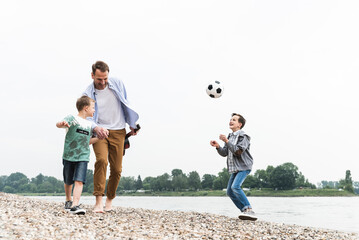 Happy father with two sons and football walking at the riverside