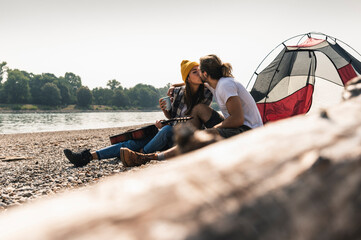 Young couple with guitar kissing at a tent at the riverside