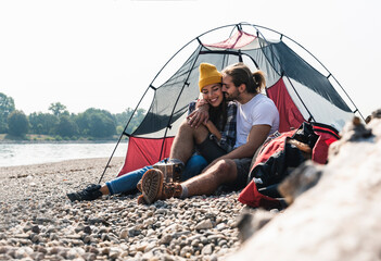 Happy young couple sitting at a tent at the riverside © tunedin