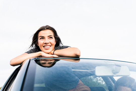 Smiling young woman looking out of sunroof of a car