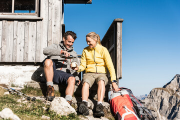 Hiking couple sitting in front of mountain hut, taking a break