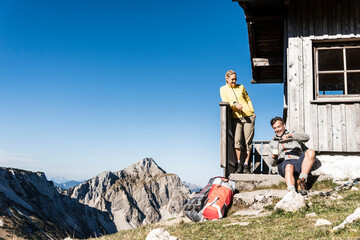 Hiking couple sitting in front of mountain hut, taking a break