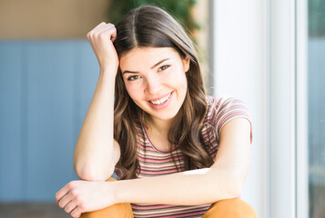 Portrait of smiling young woman sitting at the window at home