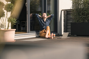 Young woman with closed eyes sitting on terrace at home with laptop