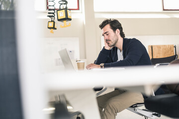 Overworked businessman sitting in office, sleeping in front of laptop