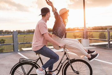 Happy young couple together on a bicycle on parking deck at sunset