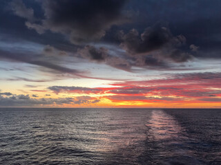 Fototapeta premium Sunset at sea, sun setting at sea, calm, ocean, path on the water from a ship, peace, landscape, horizon. Background, wallpaper