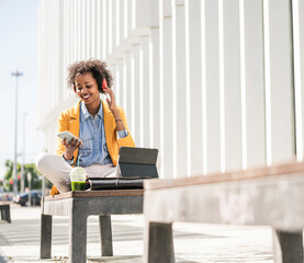 Smiling young woman with headphones, smartphone and tablet in the city