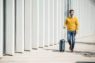 Young man with rolling suitcase and earphones in the city on the go