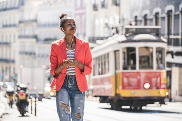 Young woman with earphones and smartphone looking around in the city, Lisbon, Portugal