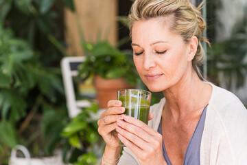 Portrait of mature woman with eyes closed with glass of green smoothie
