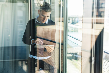 Male professional working over digital tablet while standing in office seen through window