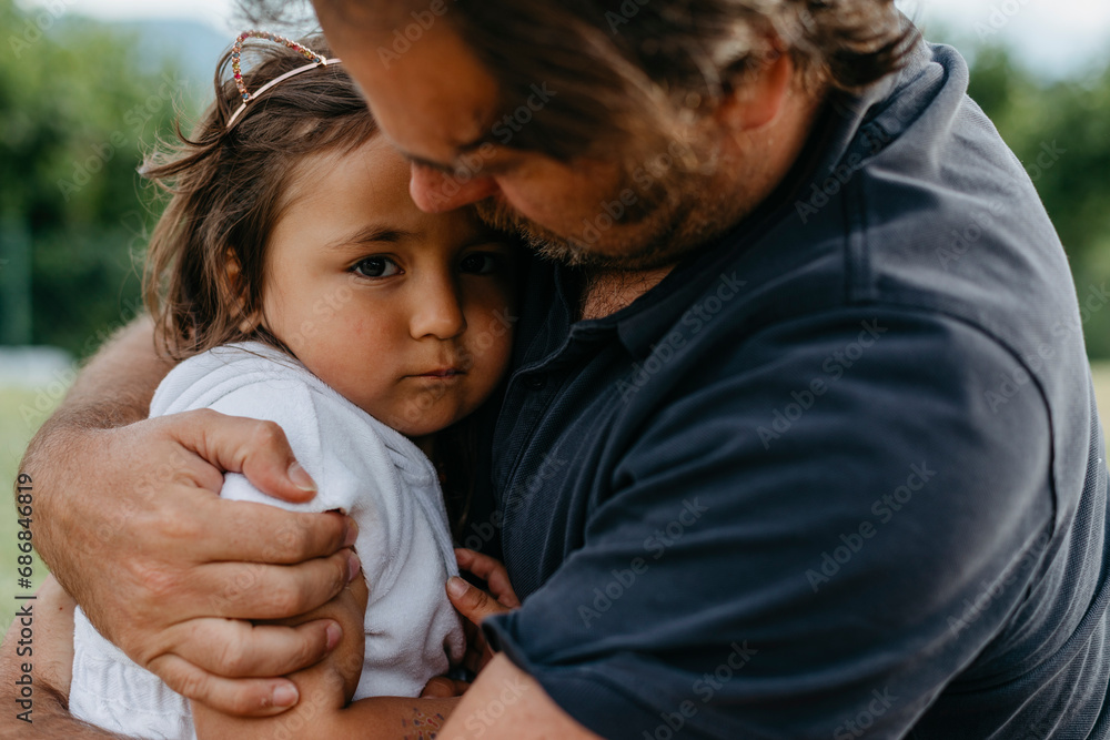 Wall mural Father embracing daughter while sitting at backyard