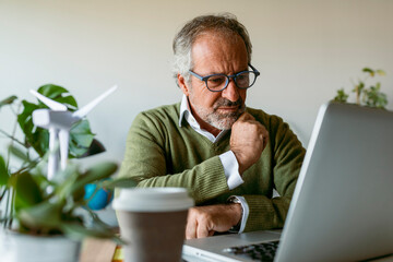 Man wearing eyeglasses using laptop while sitting by table at home