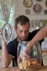 Man sitting in kitchen, looking in cookie jar, taking cokkie