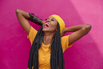 Portrait of woman with long dreadlocks laughing in front of a pink wall