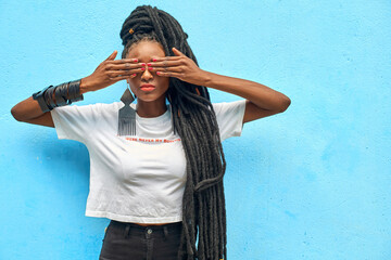 Portrait of woman with long dreadlocks covering her eyes in front of turquoise wall