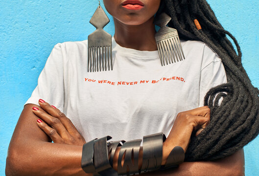 Portrait of woman with long dreadlocks wearing a T-shirt with the 'You were never my boyfriend' message on it in front of turquoise wall