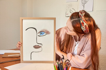 Female artist showing drawing art picture frame against wall at home