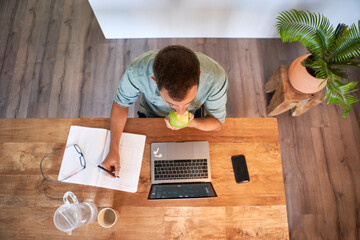 Fototapeta na wymiar Male freelancer eating fresh apple while working at home