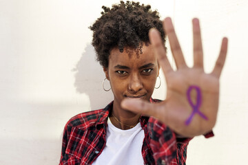 Confident young woman showing purple awareness symbol on palm against white wall during Womens Day