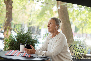 Senior woman at an outdoor cafe with cell phone and earphones