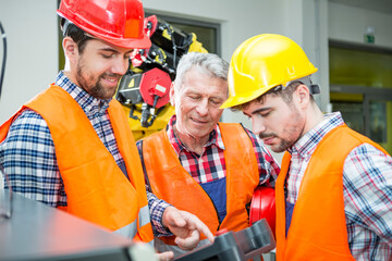 Three men in factory talking with industrial robot in background