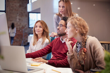 Colleagues looking over shoulder of young man working in modern office