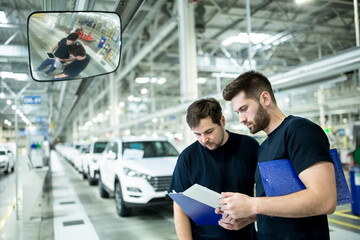 Two colleagues working in modern car factory using clipboard and tablet