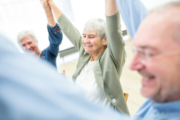 Group of seniors practicing chair gymnastics with instructor in retirement home - obrazy, fototapety, plakaty