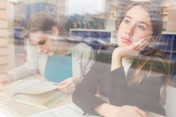 Portrait of daydreaming teenage girl in a public library looking out of window