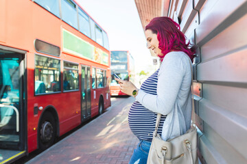 Pregnant woman using her phone at bus stop