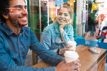 Portrait of smiling young woman in a coffee shop looking at young man - obrazy, fototapety, plakaty