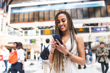 Portrait of happy young woman at train station using smartphone, London, UK - obrazy, fototapety, plakaty
