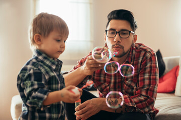 Father and son blowing soap bubbles at home