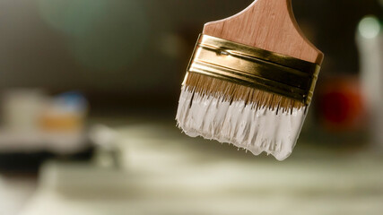 The close up shot shows a paintbrush a construction brush with white paint on the pile. It is used...