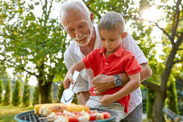 Grandfather helping grandson turning a corn cob during a barbecue in garden