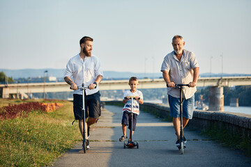 Grandfather, father and son riding scooters at the riverside