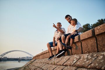 Grandfather, father and son sitting on a wall at the riverside