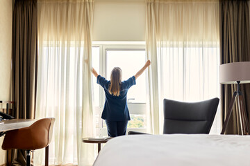 Chambermaid opening curtains of window in hotel room