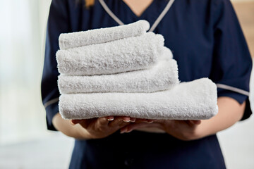Close-up of chambermaid holding towels in hotel bedroom - obrazy, fototapety, plakaty