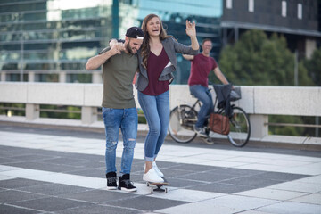 Young man supporting laughing girlfriend on skateboard