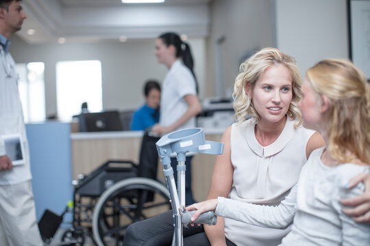 Girl with crutches sitting with her mother in reception area - Powered by Adobe