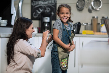 Mother tying apron for daughter in kitchen