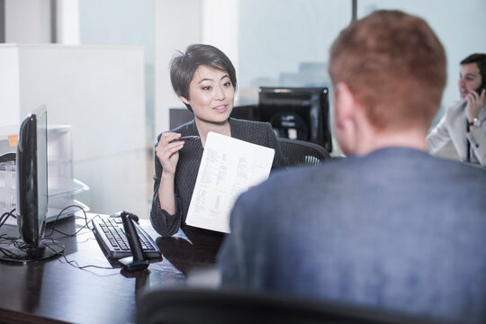 Woman showing sheet of paper to man at desk in office