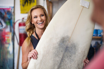 Surfboard shaper workshop, female employee smiling with surfboard