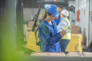 Woman wearing hard hat writing on clipboard in factory