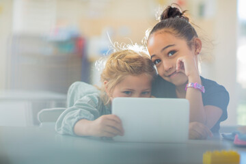 Portrait of two smiling girls sharing mini tablet in kindergarten - obrazy, fototapety, plakaty