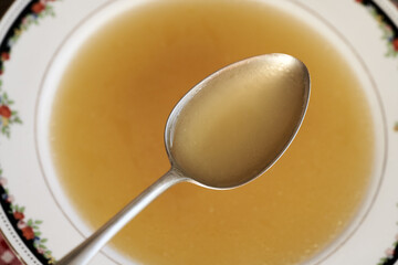 Chicken soup on a spoon above a plate, top view
